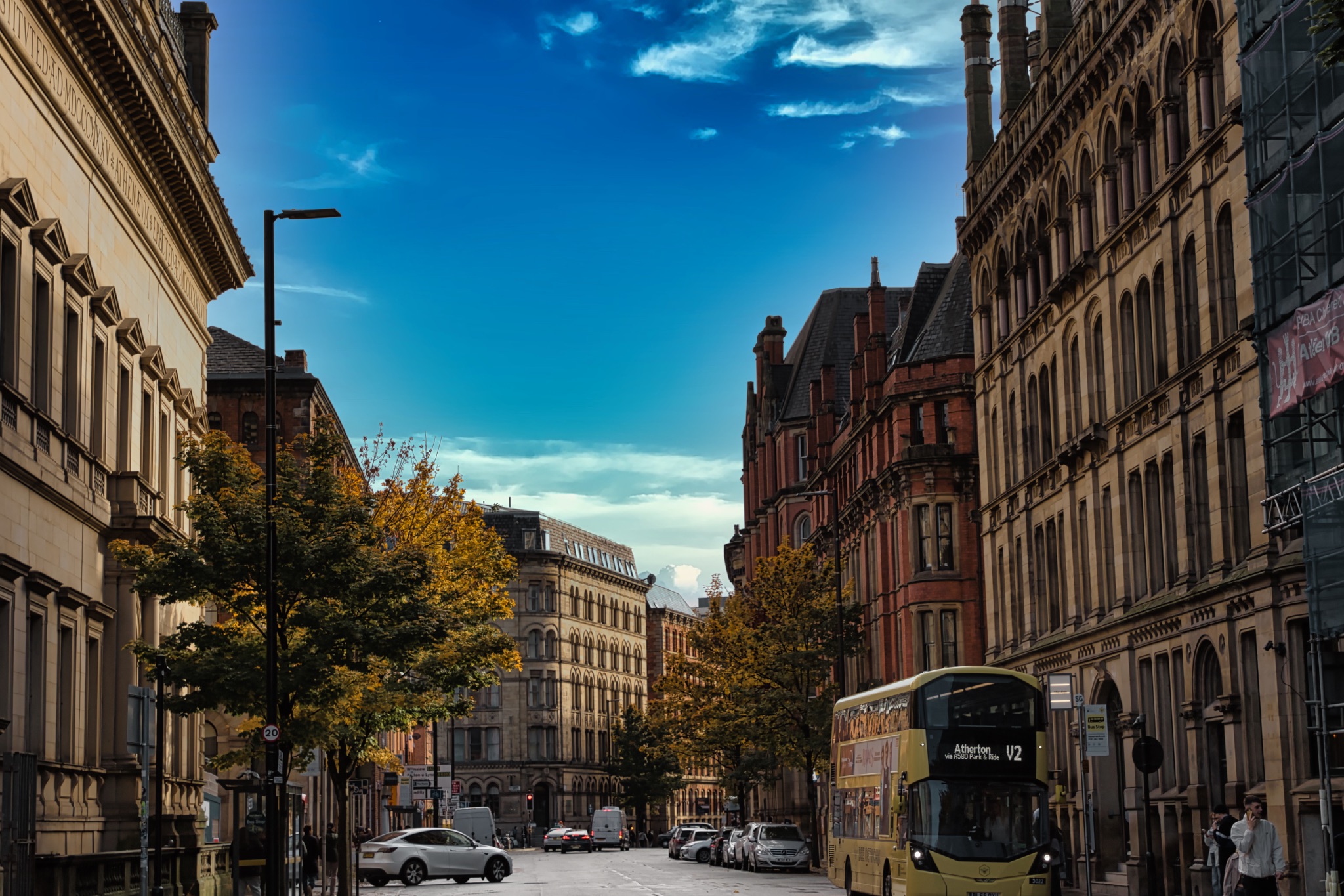 Double-Decker Bus on a City Street with Tall Brick Buildings in Manchester, UK.